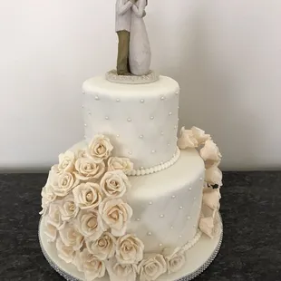 Eedding cake, with ivory colored,sugar handmade flowers, decorated with white pearls and topped with a broom and bride topper !