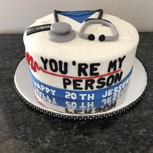 Grey&apos;s Anatomy themed cake, topped with a stethoscope and decorated with lab coat and quotation, &quot;You&apos;re my person&quot; ‍
