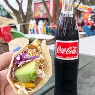 a hand holding a taco and a bottle of coke