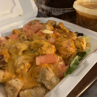 a takeout container filled with chicken, cheese, tomatoes, and lettuce