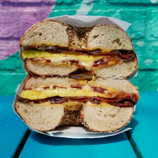 Our Bacon Sun City bagel sandwich, cut in half to show the fluffy bodega-style eggs, crispy bacon, melty cheese, and chewy Everything bagel.