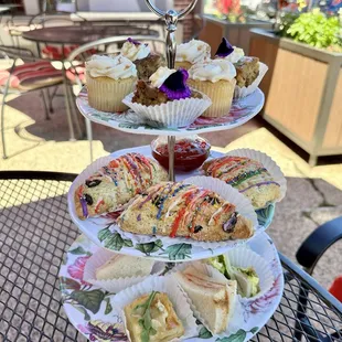 Three tiered tray with desserts on top, scones in the middle, &amp; finger sandwiches on the bottom.