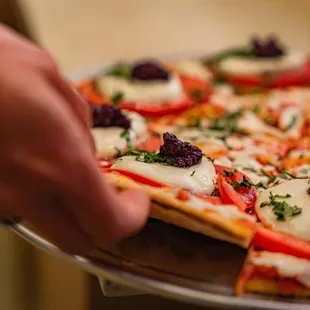 a hand grabbing a piece of pizza