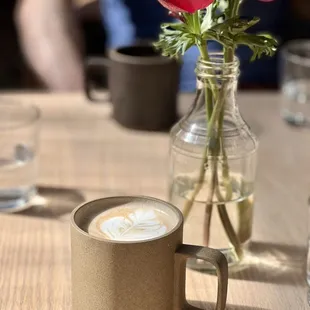 a cup of cappuccino and a vase of flowers