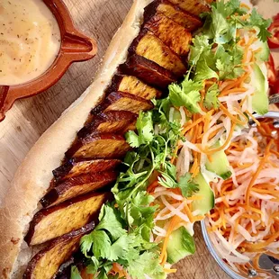 Plant Based Baked Marinated Tofu Banh Mi with fresh in-house baked baguette, cucumbers, house made pickled carrots daikon, cilantro