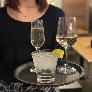 a woman in a face mask holding a tray with glasses of wine