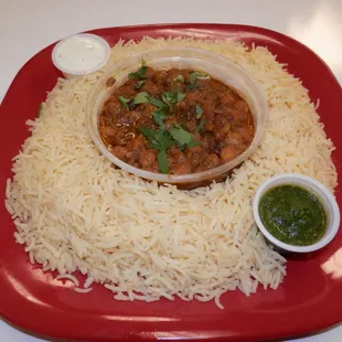 a red plate with rice and a bowl of sauce