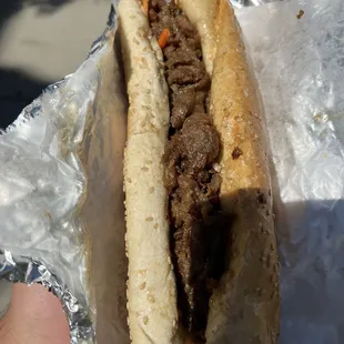 a hand holding a sandwich wrapped in tin foil