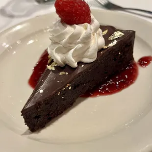 From the 2023 holiday musical show special menu: Course 5 -- flourless chocolate cake with gold fleck, whipped cream, and raspberry coulee