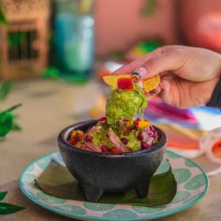a hand dipping a tortilla into a bowl of guacamole