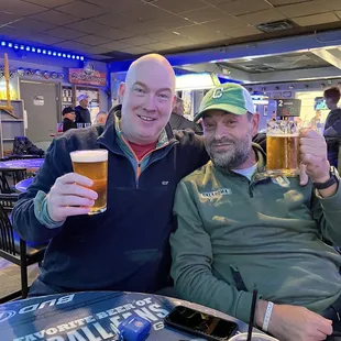 two men sitting at a table with beers