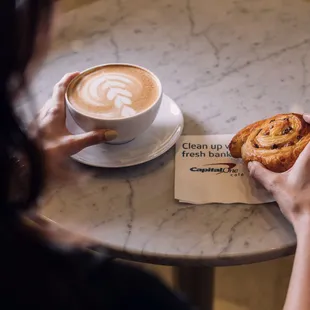 a person holding a pastry and a cup of coffee