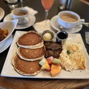 a breakfast of pancakes, eggs, fruit, and coffee