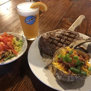 A bone-in pork chop served with a loaded baked potato and side salad