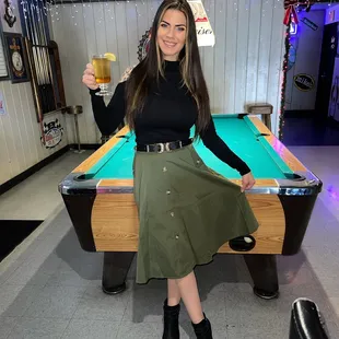a woman holding a glass of beer in front of a pool table