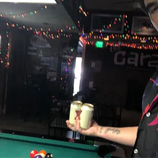 a man holding a glass of beer in front of a pool table