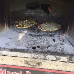 two pizzas cooking in a wood burning oven