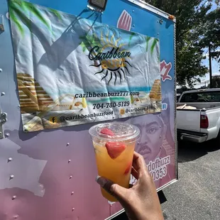 a person holding a drink in front of a food truck