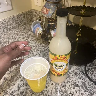 a hand holding a plastic cup next to a bottle of juice