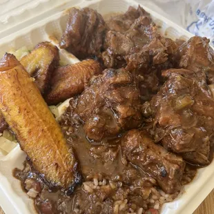 large oxtail plate with steamed vegetables, fried plantains, and rice and peas