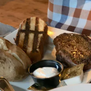 Steak, baked potato and grilled bread.