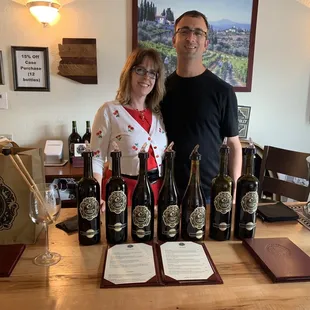 a man and woman standing in front of a table of wine bottles