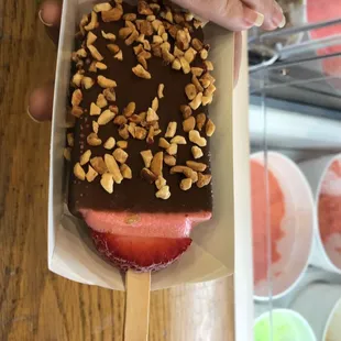 Strawberry ice cream covered in dark chocolate and rolled in peanuts.