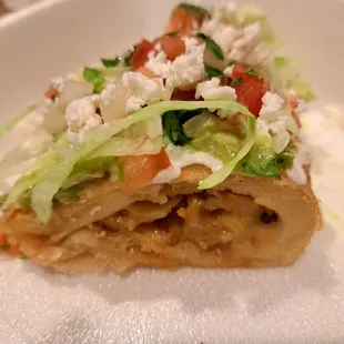 Inside half a chicken empanada topped with fresh lettuce, sour cream, guacamole, pico de gallo, queso fresco, and salsa verde
