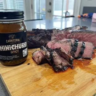 a piece of steak on a cutting board next to a jar of chili sauce