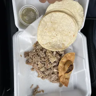 a hand grabbing a tortilla from a styrofoam container