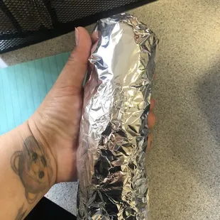 a hand holding a sandwich wrapped in aluminum foil