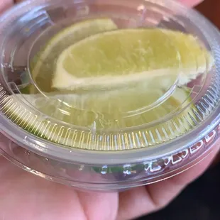 a hand holding a plastic container with a slice of lemon on it