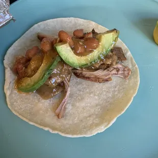 Carnitas taco with whole beans avocado and salsa on a handmade tortillas