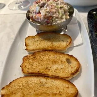 four pieces of bread on a plate with a bowl of salad in the background