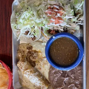 This is a Cantina Combo. It has an Enchilada, a soft taco and a tostada with a side of refried beans and green salsa.