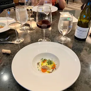 a woman sitting at a table with a plate of food and wine