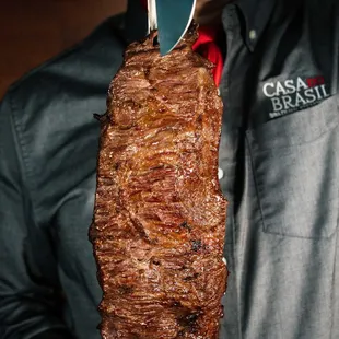 a man holding a large steak on a skewer