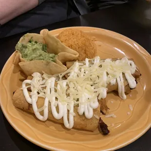 Taquitos Mexicanos: drizzled with sour cream, topped with cheese.  A side of rice and guacamole in a cute tortilla bowl.
