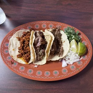 Three tacos with flour tortillas. Left to right Chorizo, Carnitas, Barbacoa