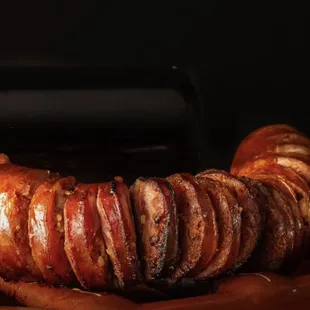 a sausage wrapped in bacon in a clay bowl with a bottle of wine in the background