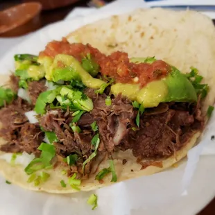 Barbacoa Taco on homemade maize with cilantro and onion added sliced aguacate.  Topped with chip salsa and a green chili sauce.
