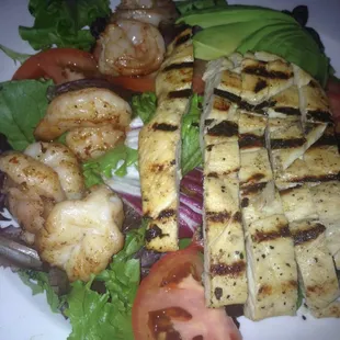Salad with chicken and shrimp topped with a whole avocado.