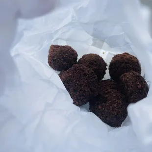 a pile of chocolate donuts in a white paper bag