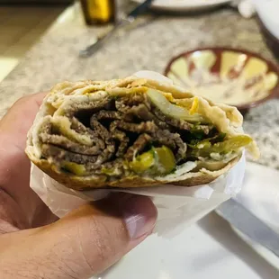 a hand holding a sandwich with meat and vegetables