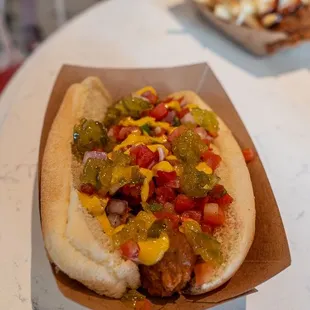 Plant-based Chicago-style Dog (Vegan) Beyond Hot Italian  "Sausage" topped with Diced Tomatoes, Onions, Yellow Mustard, and Relish
