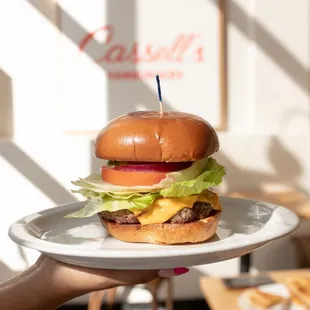 a hand holding a plate with a cheeseburger