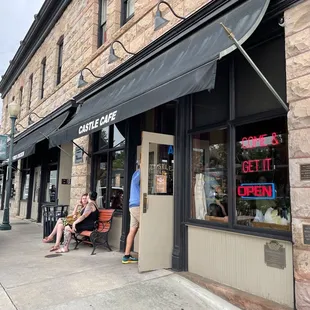 two people sitting on a bench in front of a stone building