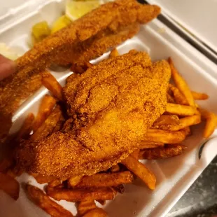 a hand holding a container of fried fish and french fries