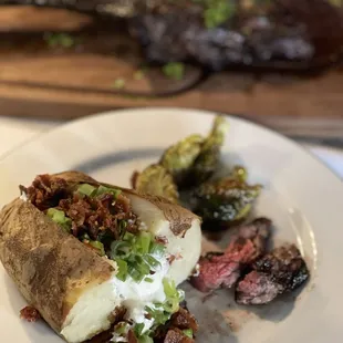 Half of a loaded baked potato, brussle sprouts &amp; pieces of tomahawk steak