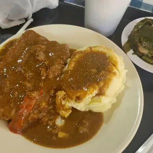 Meatloaf with mashed potatoes and gravy, with a side of mustard greens.